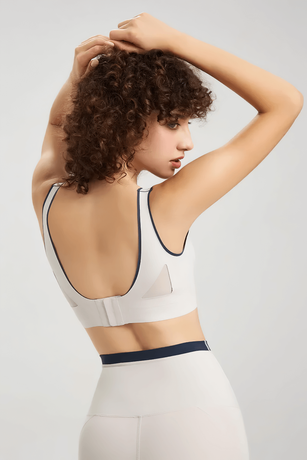 Back view of a woman in a seamless white sports bra showcasing breathable stretch design, ideal for yoga and running, with secure button closure.